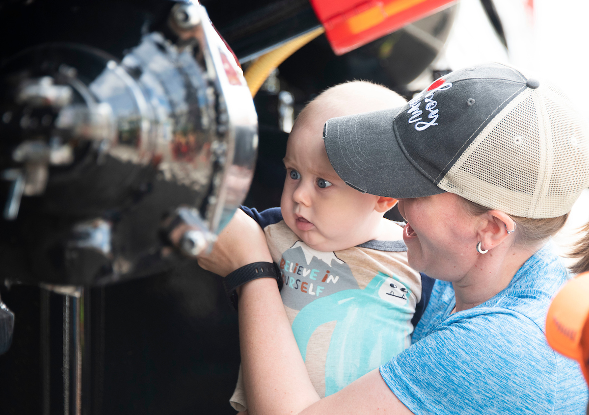 A baby touches truck parts while a smiling parent holds them up. 